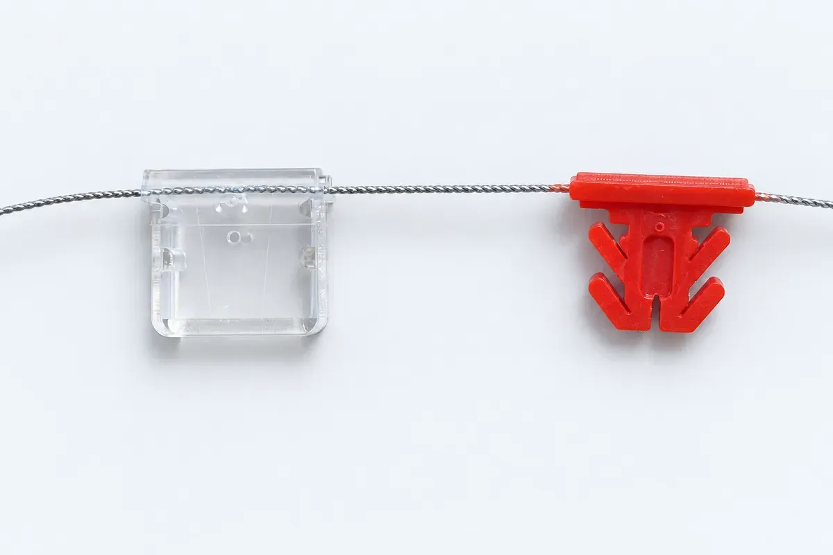 Meter seal sample with a transparent housing on the left and a red inner component on the right, separated on steel wire